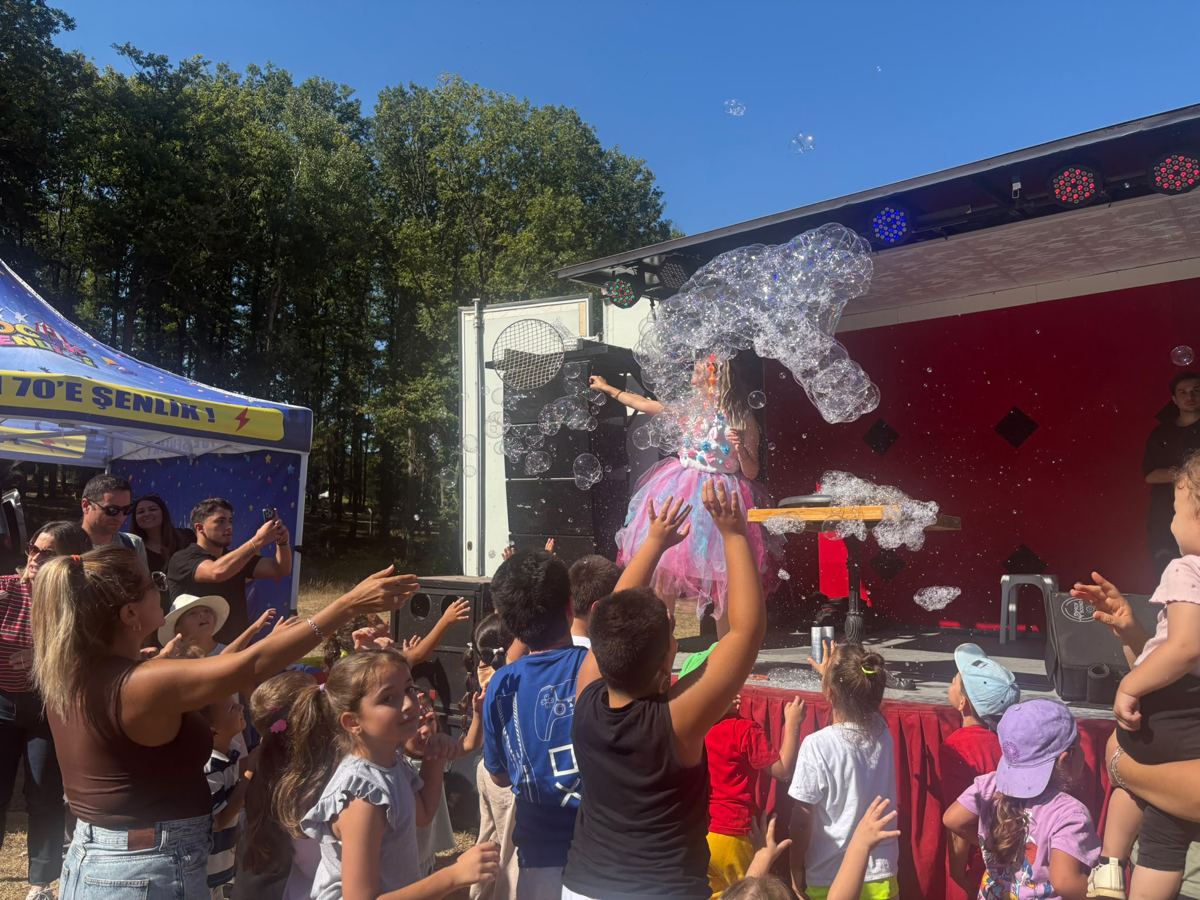 Festival sahnesinde bubble show sırasında köpüklere uzanan çocuklar